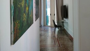 A hallway with a large abstract painting, a glass table with a chair, and a TV on the wall. - Duomo156 (Messina)