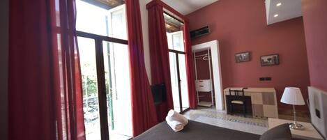 A hotel room with a bed, a desk, a chair, a wardrobe, and a window with red curtains.