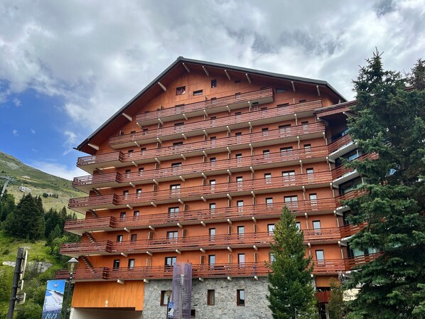 A multi-story hotel with balconies, a stone facade, and a mountainous backdrop.