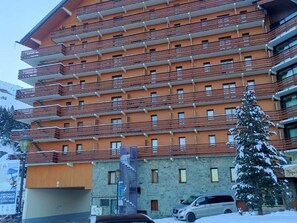 A multi-story hotel with balconies, a stone facade, and a parking area.