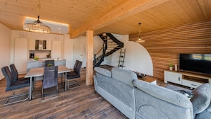 A modern interior with a dining area, sofa, staircase, and TV. - Vacation home "Juist" with 105sqm - in the vacation park Harkebrügge (Barßel)