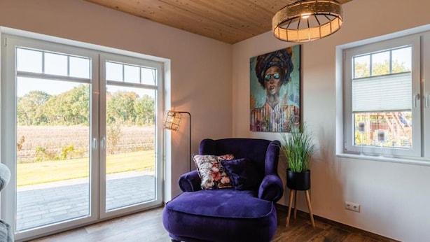 A room with a purple armchair, a painting, a floor lamp, and a potted plant. - Vacation home "Juist" with 105sqm - in the vacation park Harkebrügge (Barßel)