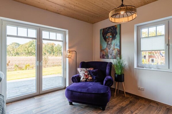 Um quarto com uma poltrona roxa, um quadro, um abajur e um vaso de planta.