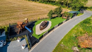 An aerial view of a playground with a slide, climbing structure, and a boat-shaped play area surrounded by a fence. - Vacation home "Juist" with 105sqm - in the vacation park Harkebrügge (Barßel)