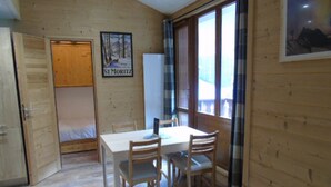 A room with a wooden floor, a bed, a table with chairs, a window with curtains, and a poster on the wall. - Renovated 3-room comfort apartment, balconies, near lifts, Wifi, pets allowed (Valfréjus)