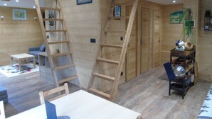A room with wooden walls, a loft area, a ladder, a table, and a shelf with items. - Renovated 3-room comfort apartment, balconies, near lifts, Wifi, pets allowed (Valfréjus)
