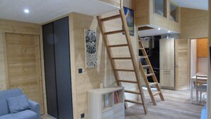A loft-style room with a wooden floor, a bookshelf, a grey sofa, and a ladder leading to an upper level. - Renovated 3-room comfort apartment, balconies, near lifts, Wifi, pets allowed (Valfréjus)