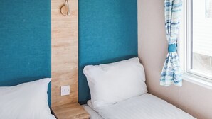 Ein Schlafzimmer mit zwei Einzelbetten, einem Nachttisch aus Holz, einer Wandleuchte und einem Fenster mit Vorhängen.