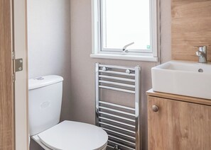 A small bathroom with a toilet, a towel rack, a window, and a sink. - Otterton Premier Plus 3 (Budleigh Salterton)