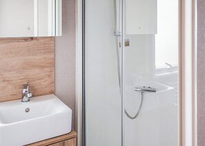 Ein modernes Badezimmer mit einer Duschkabine aus Glas, einem weißen Waschbecken und einem hölzernen Waschtisch.