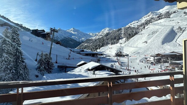 Paisaje montañoso nevado con pistas de esquí, un telesilla y un edificio con techo inclinado.