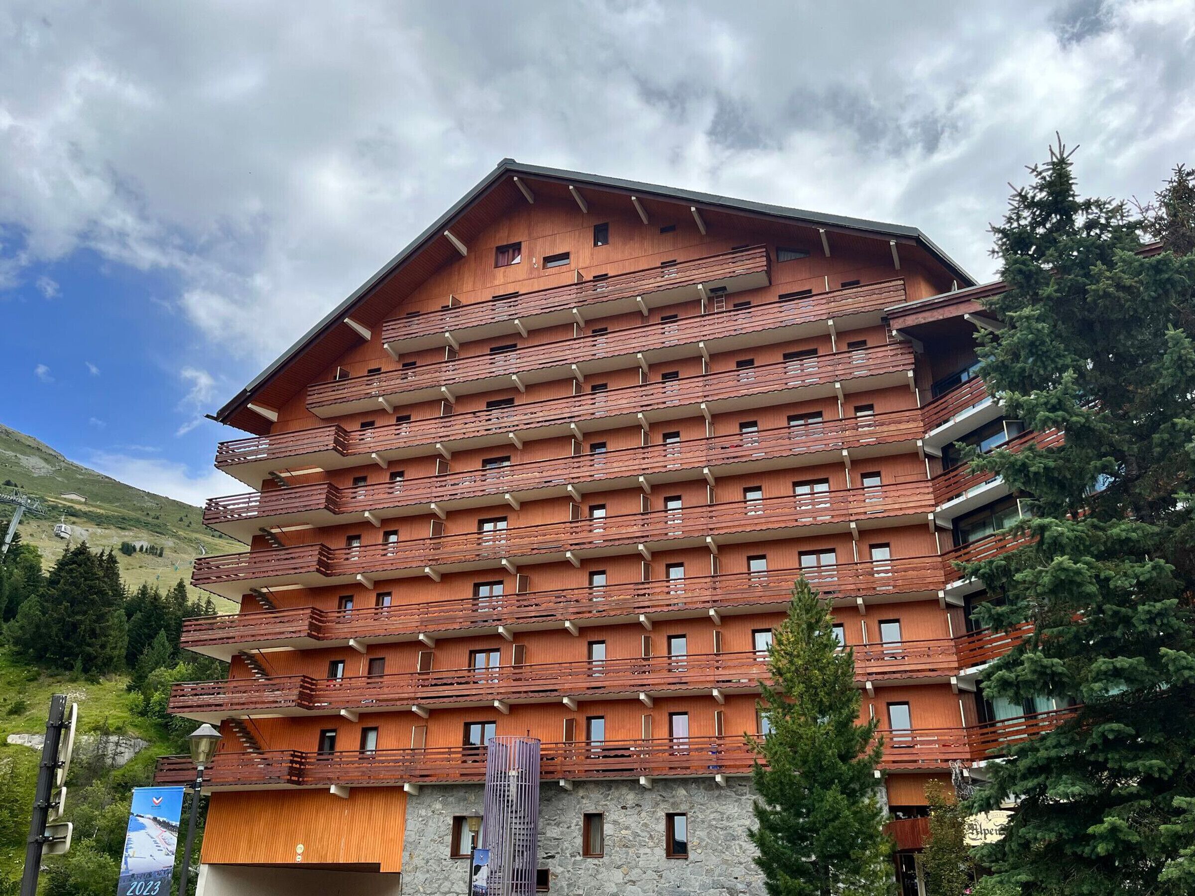 A multi-story hotel with balconies, a stone facade, and a mountainous backdrop.