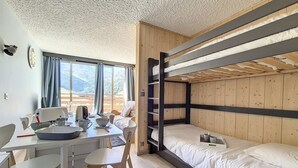 Habitación pequeña con literas, una mesa de comedor con sillas y vistas a las montañas desde la ventana.