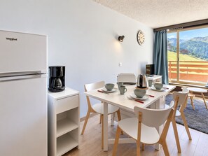 A modern kitchen with a refrigerator, coffee maker, and dining area with chairs and table.
