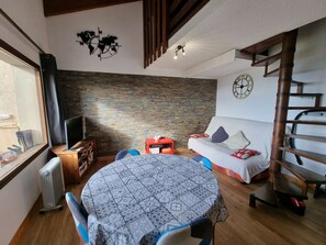 Una sala de estar acogedora con una pared de piedra, una mesa redonda, un sofá, un televisor y una escalera de madera.