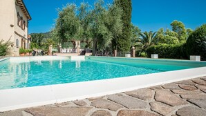 Una piscina con baldosas de piedra, rodeada de árboles y un edificio con techo inclinado.