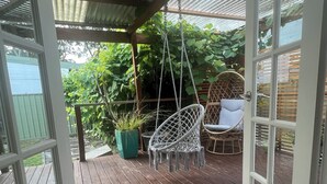 Une terrasse en bois ouverte, avec un fauteuil suspendu, un fauteuil rembourré et un tapis tissé.