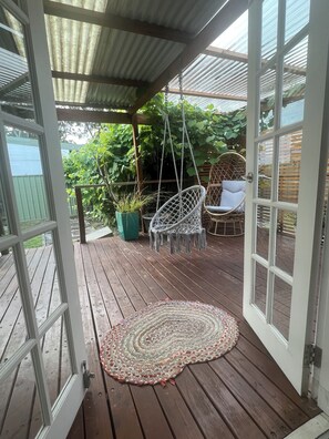 Een open houten terras met een hangstoel, een stoel met kussens en een geweven vloerkleed.