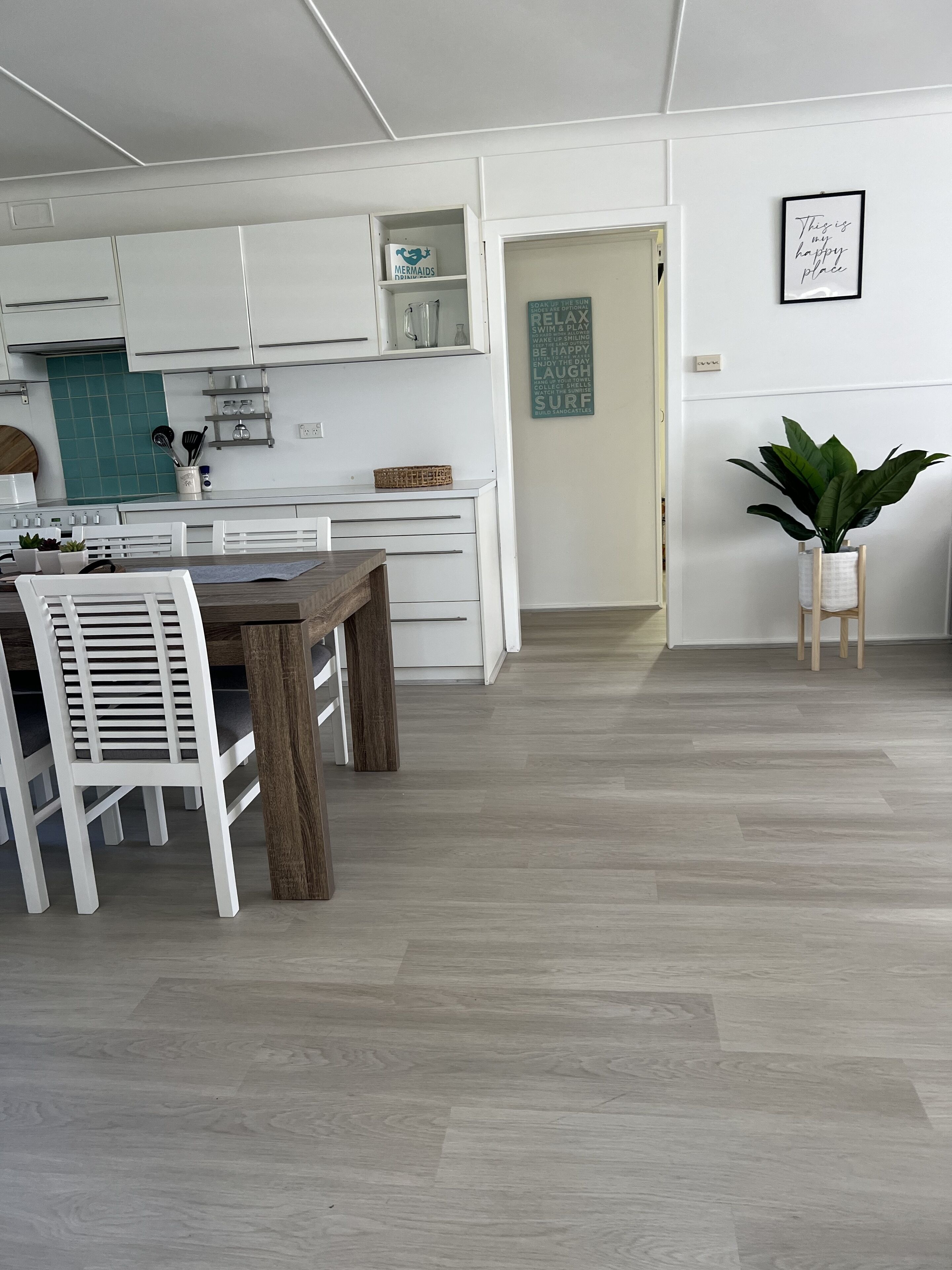 A modern kitchen with white cabinets, a dining table with white chairs, and a wooden floor.