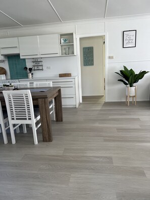 Een moderne keuken met witte kasten, een eettafel met witte stoelen en een houten vloer.