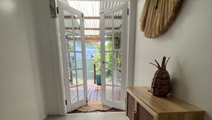 Une pièce dotée d’un grand tapis tissé, d’une console en bois et d’une porte donnant sur un espace extérieur avec une terrasse en bois et de la verdure.
