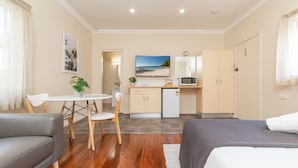 A compact hotel room with a bed, a sofa, a dining area with a table and chairs, a kitchenette, and a bathroom. - Pacific Motel 01 - Free WiFi (Forster)
