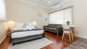 A hotel room with a bed, a grey sofa, a small table with chairs, and a potted plant. - Pacific Motel 01 - Free WiFi (Forster)