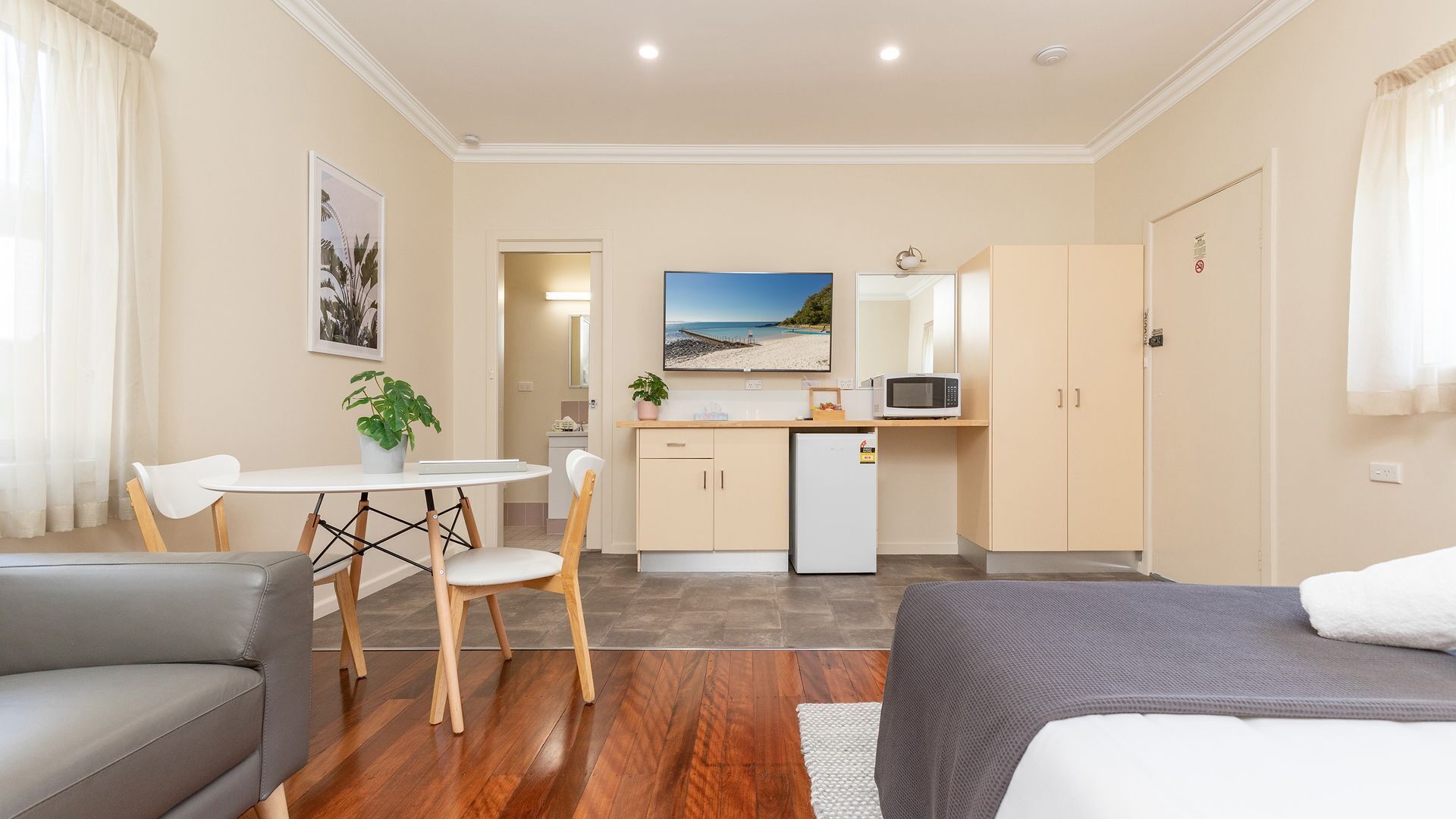 A compact hotel room with a bed, a sofa, a dining area with a table and chairs, a kitchenette, and a bathroom.