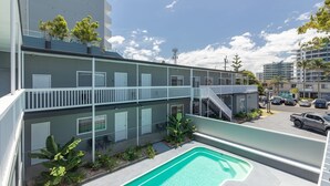 Un edificio de varios pisos con piscina en la azotea, balcones y un estacionamiento.