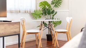 A modern living room with a round white table, two wooden chairs with white cushions, a potted plant, and a wooden cabinet. - Pacific Motel 08 - Free WiFi (Forster)