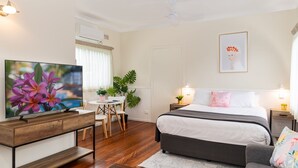 A modern hotel room with a large flat-screen TV, a bed with white linens, a gray sofa, a small round table with chairs, and a potted plant. - Pacific Motel 08 - Free WiFi (Forster)