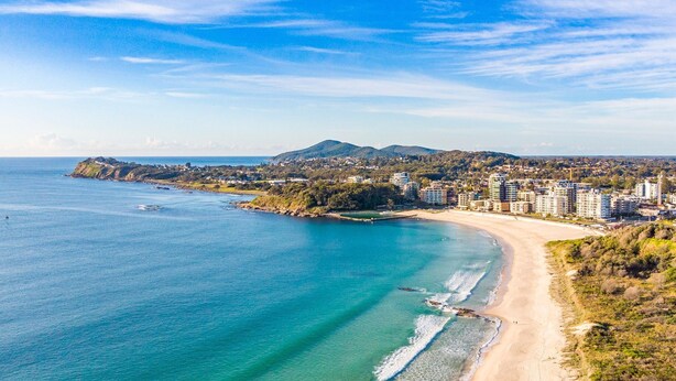 A coastal cityscape with a beach, buildings, and a mountain in the background. - Pacific Motel 08 - Free WiFi (Forster)