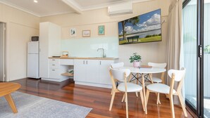 A modern kitchen with white cabinets, a wooden countertop, and a dining area with a round table and chairs. - Jasmine Lodge in the heart of Forster (Forster)