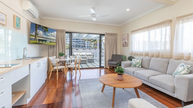 A modern living room with a sofa, a dining table with chairs, a kitchen area, and a balcony with a view of buildings and greenery. - Jasmine Lodge in the heart of Forster (Forster)