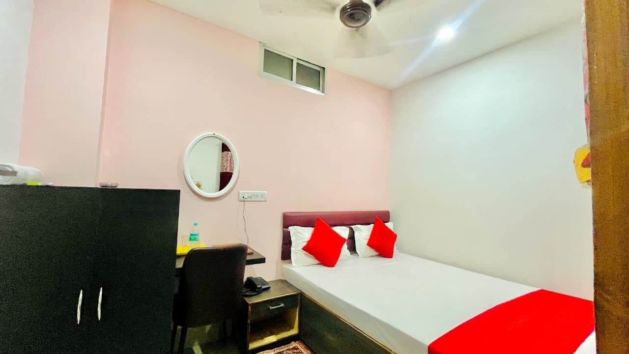 A room with a bed, a desk, a chair, a mirror, and a small window.