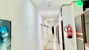 A hotel hallway with a fire extinguisher, a framed picture on the wall, and a door with a glass panel.