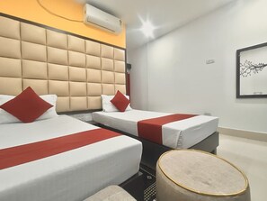 A hotel room with three beds, a tufted headboard, a round table, and a wall-mounted air conditioner.