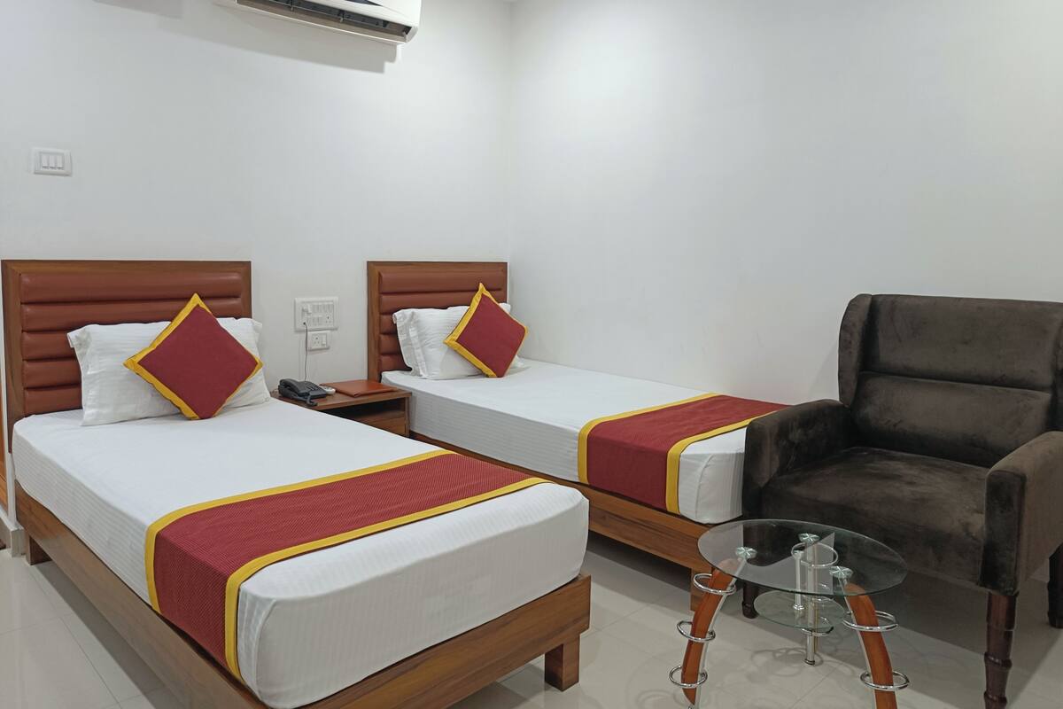 A hotel room with two single beds, a brown leather armchair, and a small glass table.