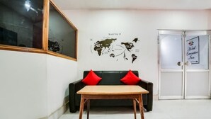 A lobby with a world map on the wall, a black leather sofa with red cushions, and a wooden table.