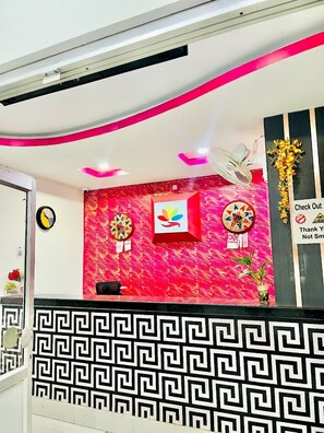 A reception area with a modern design, including a patterned wall, a reception desk, and a sign with a warning symbol. - Hotel Executive Inn (Hailakandi)
