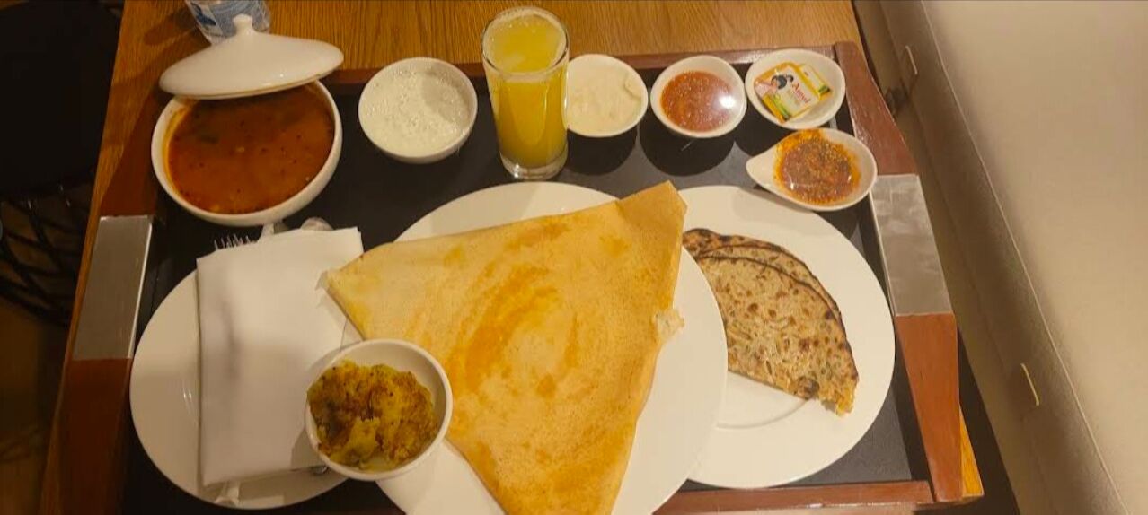 A table with a meal consisting of a large dosa, a bowl of curry, a plate of flatbread, and several small bowls of condiments.