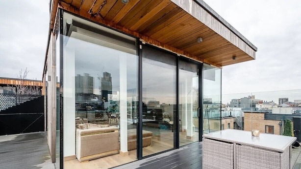 A modern rooftop terrace with glass walls, a wooden ceiling, and a seating area with a sofa and a table.