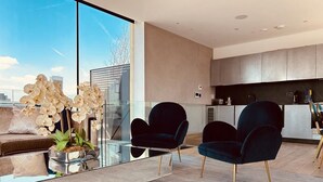 A modern living room with a glass coffee table, two dark armchairs, and a potted orchid plant.