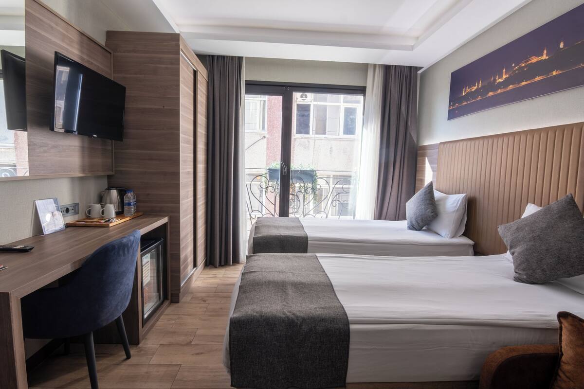 A hotel room with two beds, a desk, a TV, and a balcony with a view.