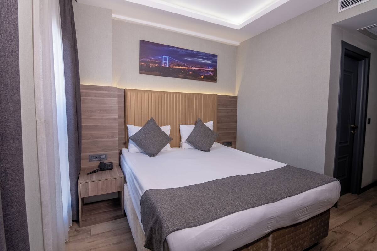 A hotel room with a bed, a nightstand, a wall-mounted picture, and a door.