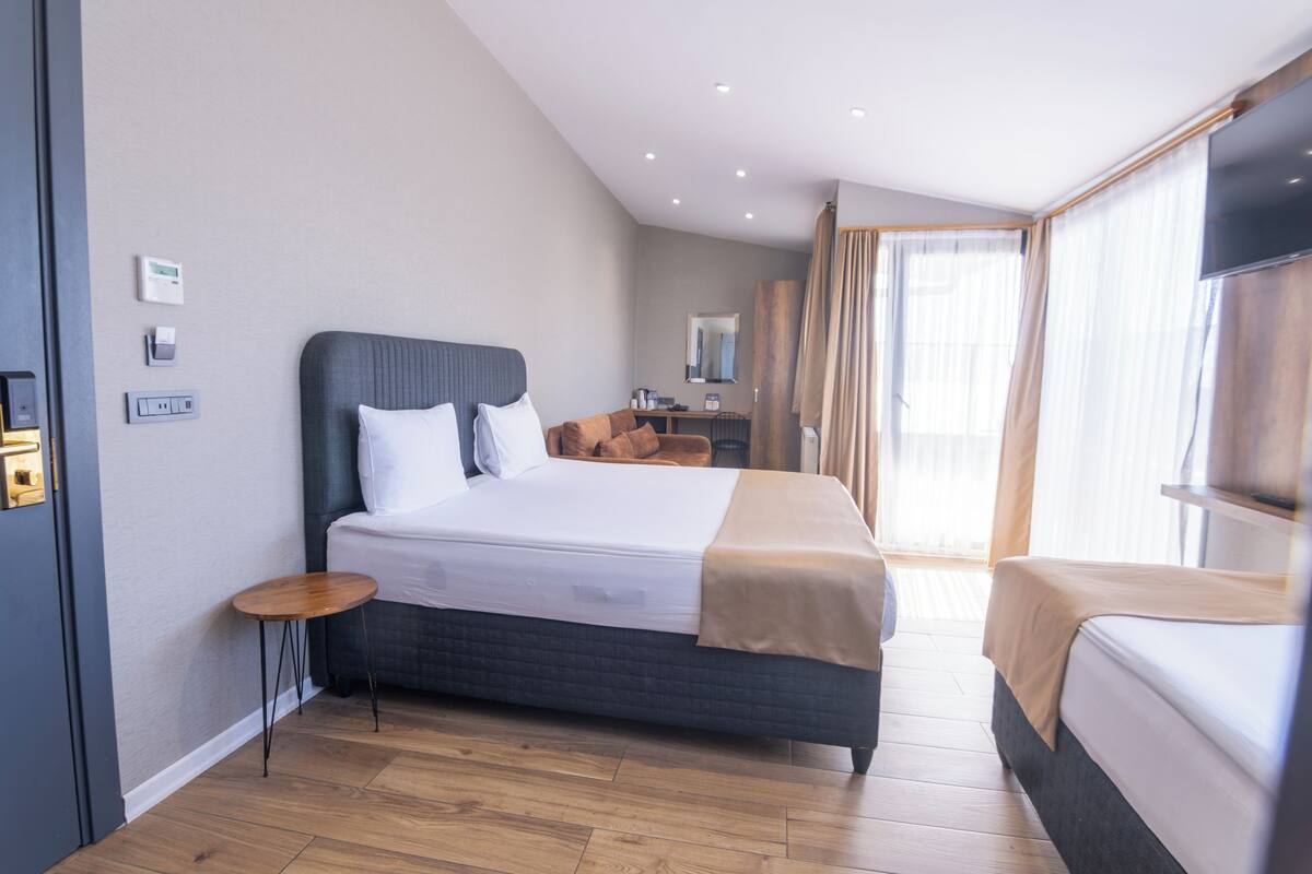 A modern hotel room with a large bed, a bedside table, a desk, and a television.