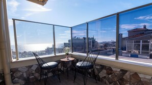 Ein Balkon mit zwei Stühlen und einem kleinen Tisch, mit Blick auf eine Stadtlandschaft, die ein Gewässer und Gebäude zeigt.