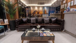 Eine moderne Lobby mit einer Ledersofa, einem Glastisch und einer Wandmalerei eines historischen Gebäudes.
