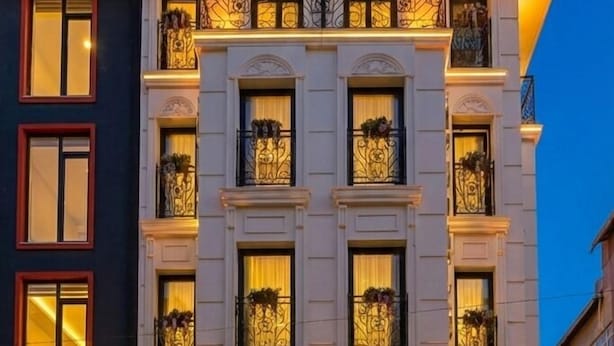 Ein mehrstöckiges Hotel mit klassischer Architektur, mit Balkonen, die mit schmiedeeisernen Geländern versehen sind, und einem Eingangsbereich auf Erdgeschossniveau mit Glasfassade.