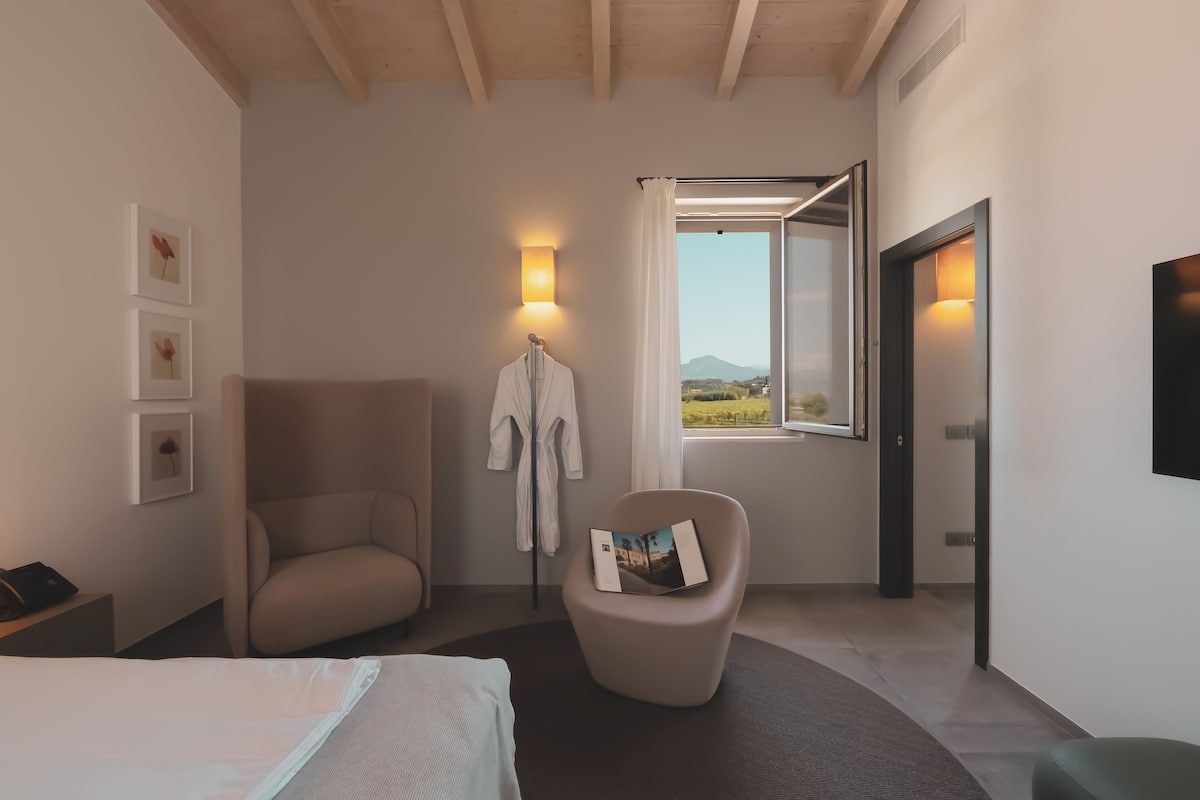 Ein modernes Hotelzimmer mit Bett, einer Couch, einem Lesesessel und einem Fenster mit Blick ins Grüne.